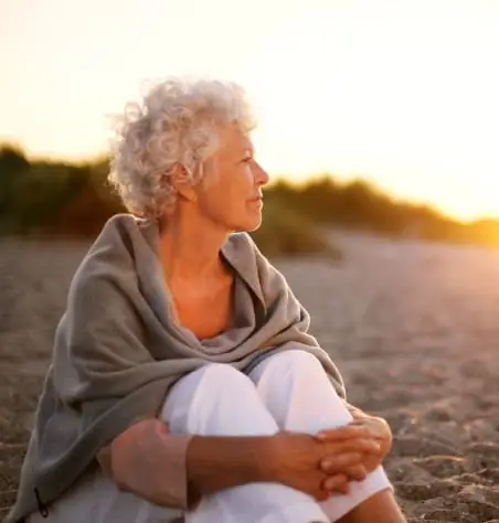 Older woman sits on a beach at sunset.