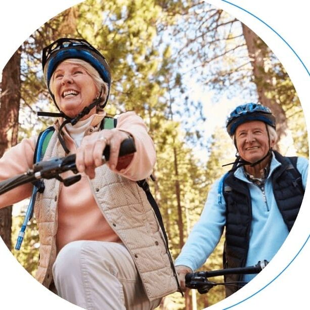 Two seniors smiling while biking in forest.